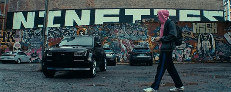 man in a pink hoodie walking towards a large black SUV