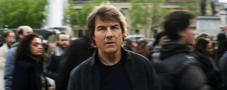 A large group of people walking through an open area with Tom Cruise in the centre of the shot looking directly into camera.